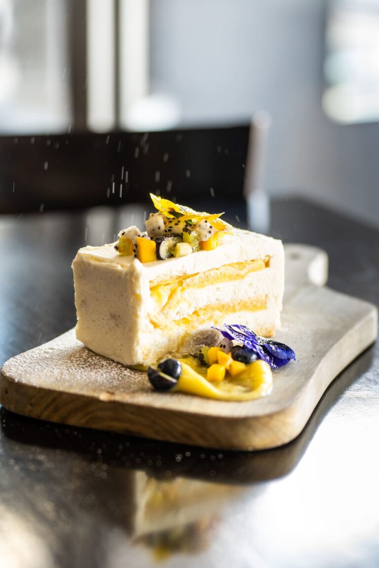 A slice of Capital Prime's Limoncello Tiramisu cake displayed on a rustic wooden board, topped with a tropical fruit relish. Award-Winning desserts