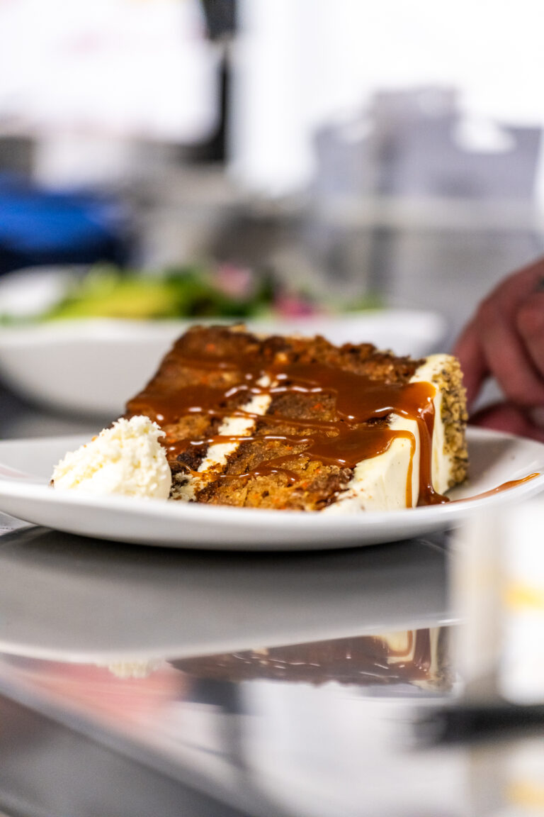 A large, delicious looking slice of Capital Prime's carrot cake topped with caramel and frosting