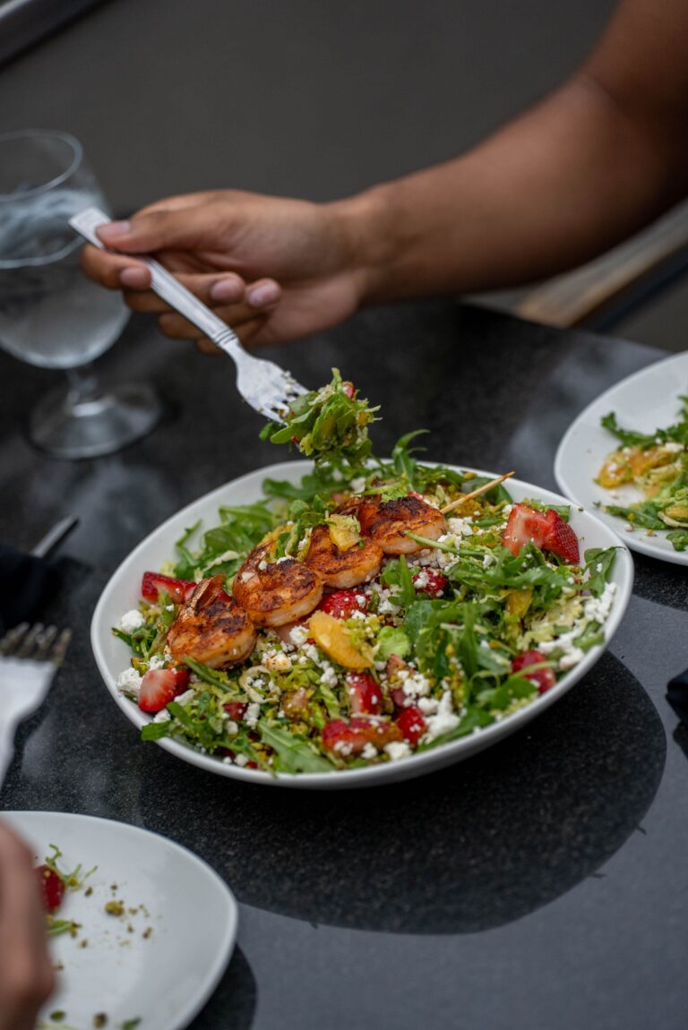 shrimp, oranges, strawberries, and feta cheese atop a pile of greens